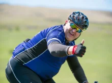 Guy giving a thumbs up while cycling with cycling glasses and a bike helmet on